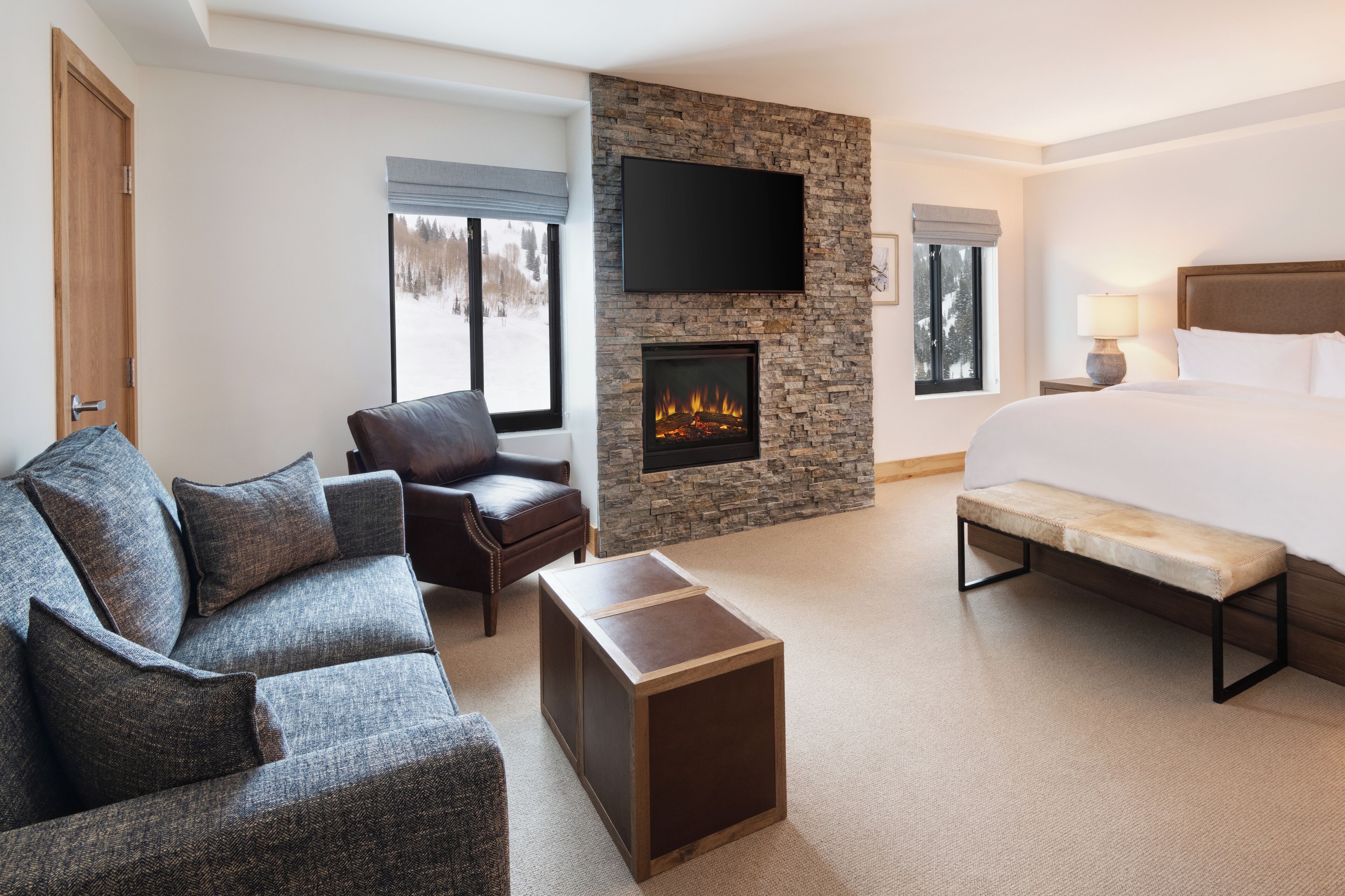 Een hotelkamer met een groot bed, een stenen openhaard, een flatscreen televisie, een leren bank en een bankje.