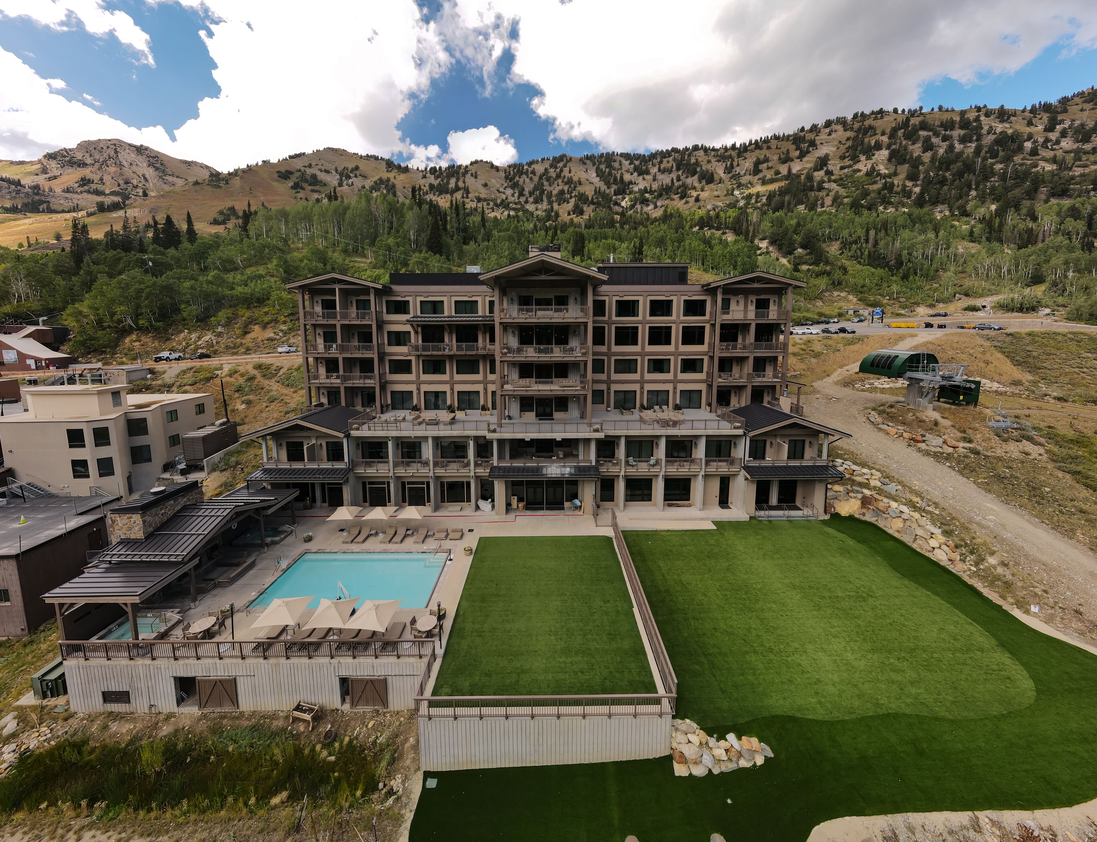 Ein mehrstöckiges Hotel mit Pool, Sitzgelegenheiten im Freien und Blick auf die umliegenden Berge.