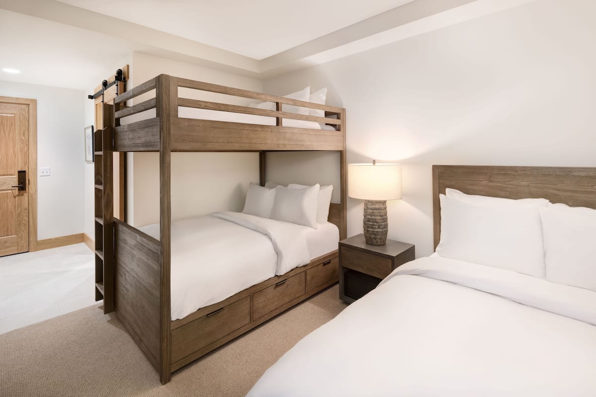 A bunk bed room with a wooden headboard, a bedside table with a lamp, and a door.