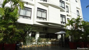 Un hotel de varios pisos con fachada blanca, grandes ventanales y zona de estar exterior con sombrillas.