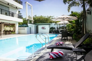 Ein Schwimmbecken mit Liegestühlen und Sonnenschirmen, ein Schild mit der Aufschrift 'Hilton' und ein Gebäude mit Balkon.
