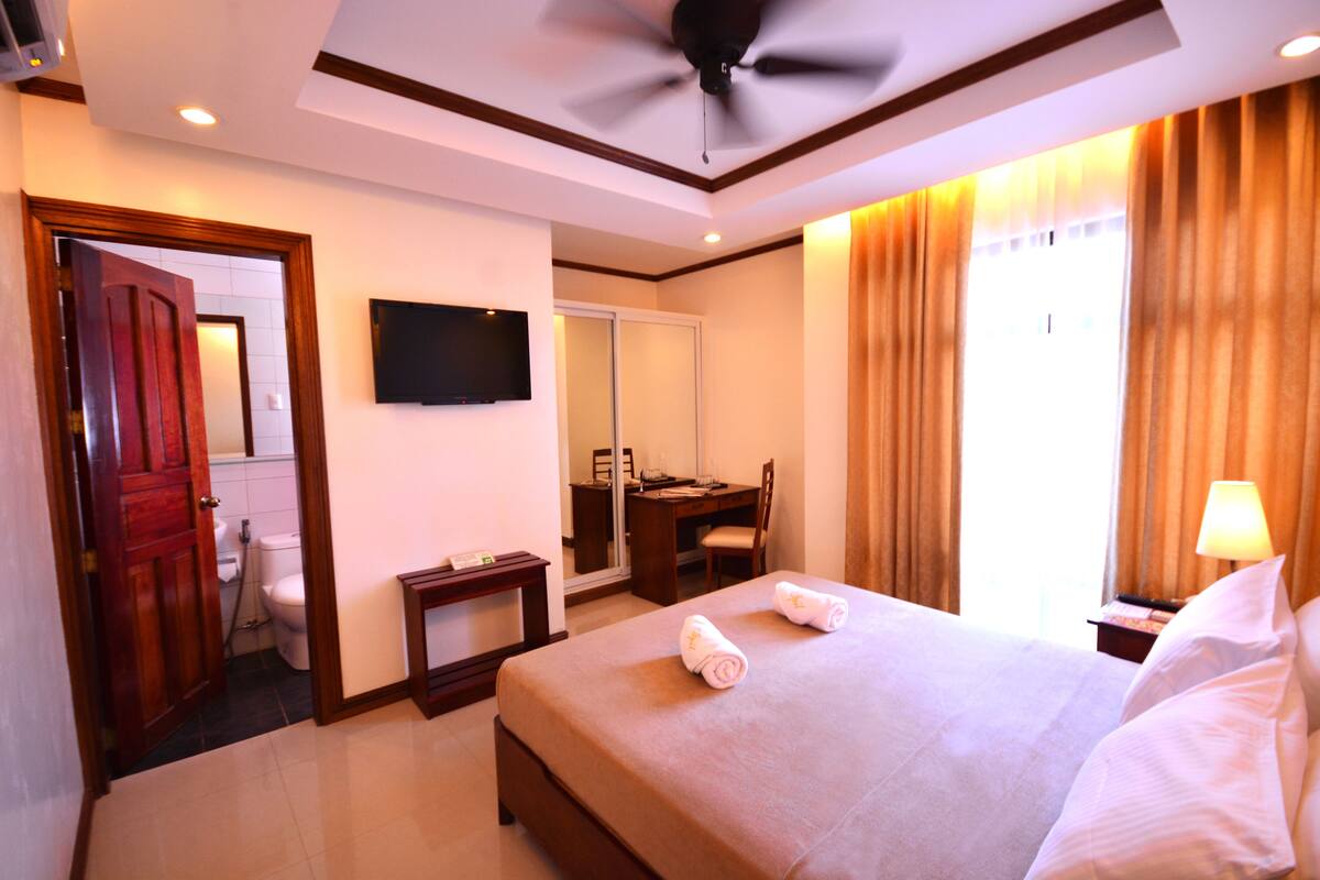 Una habitación de hotel con cama, escritorio, silla, televisor y baño.