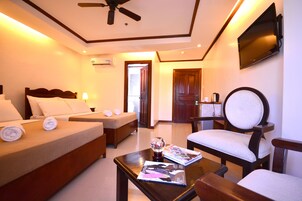 A hotel room with a bed, a sofa, a table with magazines, a TV, and a ceiling fan.