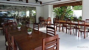 Un comedor amplio con mesas y sillas de madera, ventiladores de techo y ventanas grandes con vista a la vegetación.