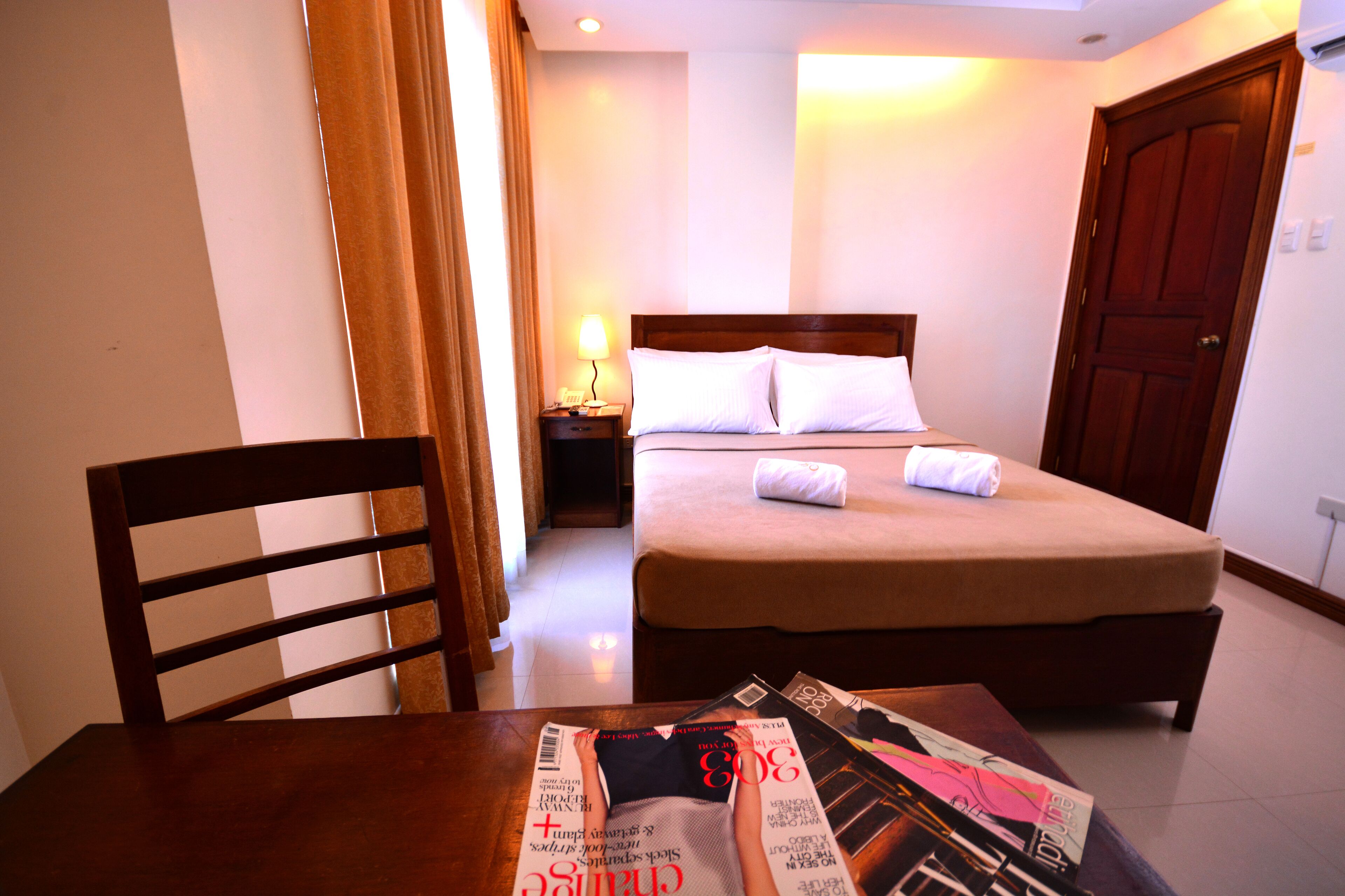 Une chambre d’hôtel avec un lit, une table de chevet, une table avec des magazines et une chaise.