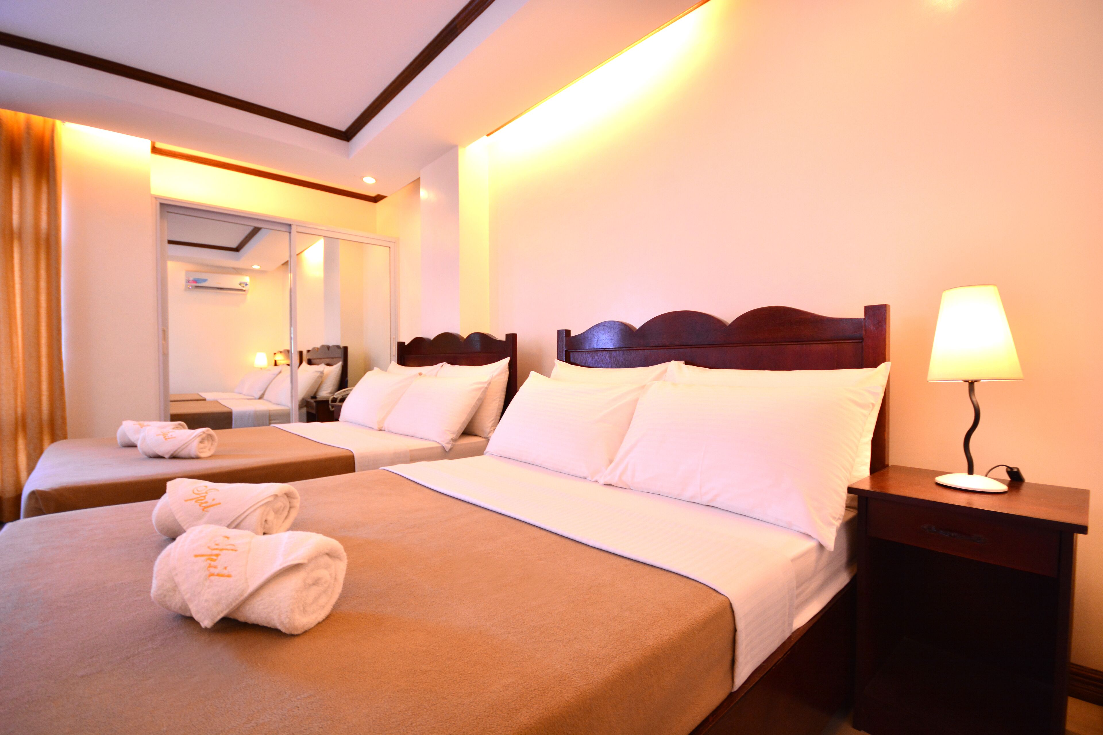 A hotel room with two beds, a nightstand with a lamp, and a mirror.