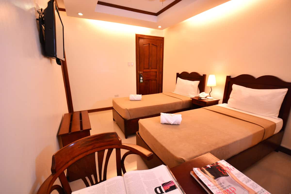 Habitación de hotel con dos camas, un escritorio, una silla, un televisor y una puerta.