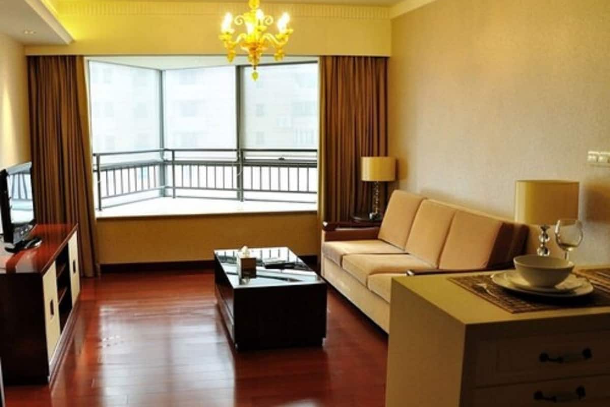 Une chambre d’hôtel avec une grande fenêtre, un canapé, une table basse, une télévision et un lustre.