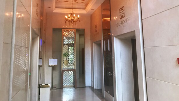 Un pasillo con candelabro, paredes de azulejos y una puerta de cristal con un letrero.