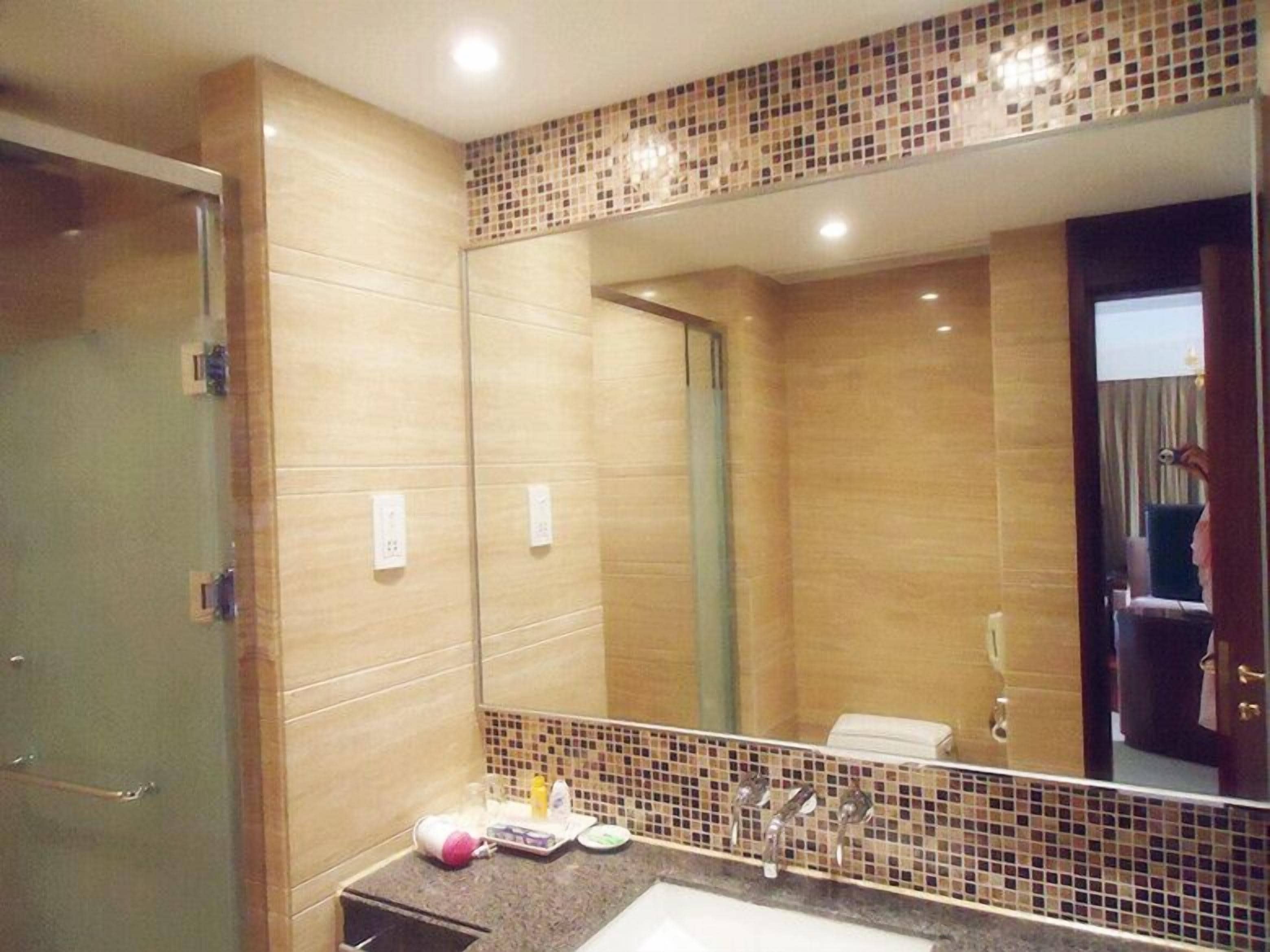 A bathroom with a large mirror, a sink with a tiled backsplash, and a shower area.