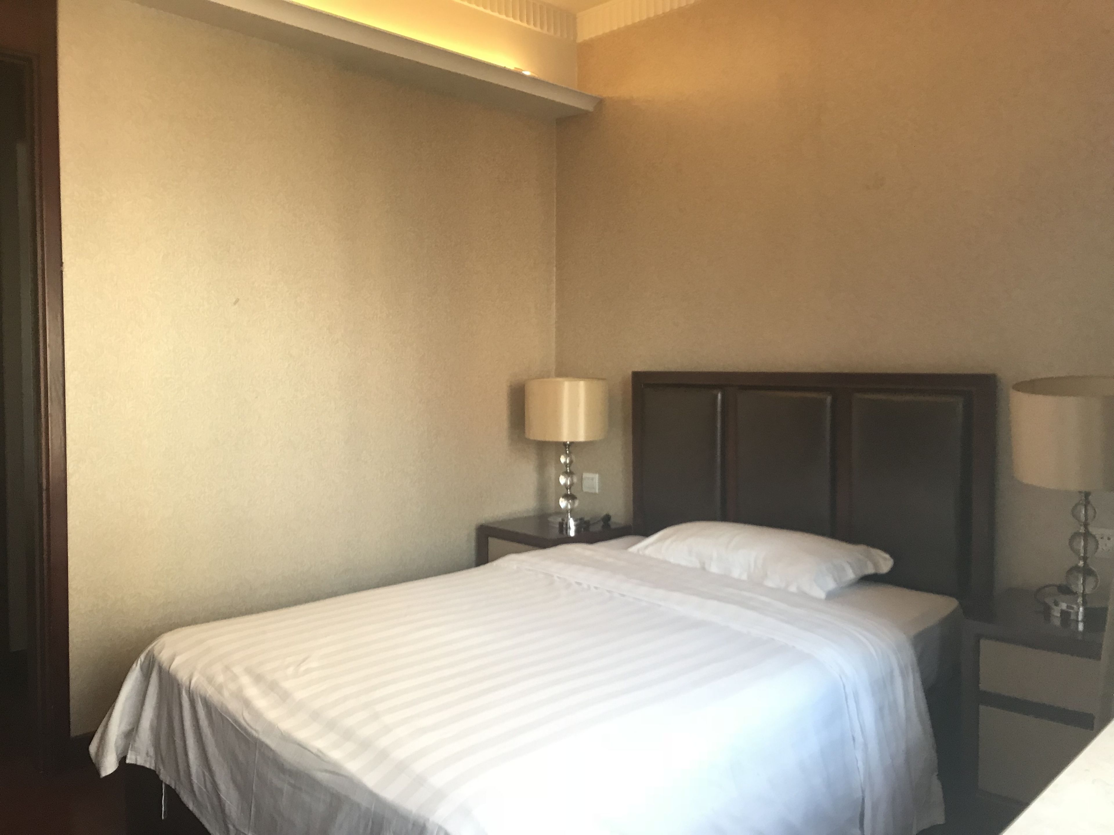 A hotel room with a single bed, a nightstand with a lamp, and a dresser.