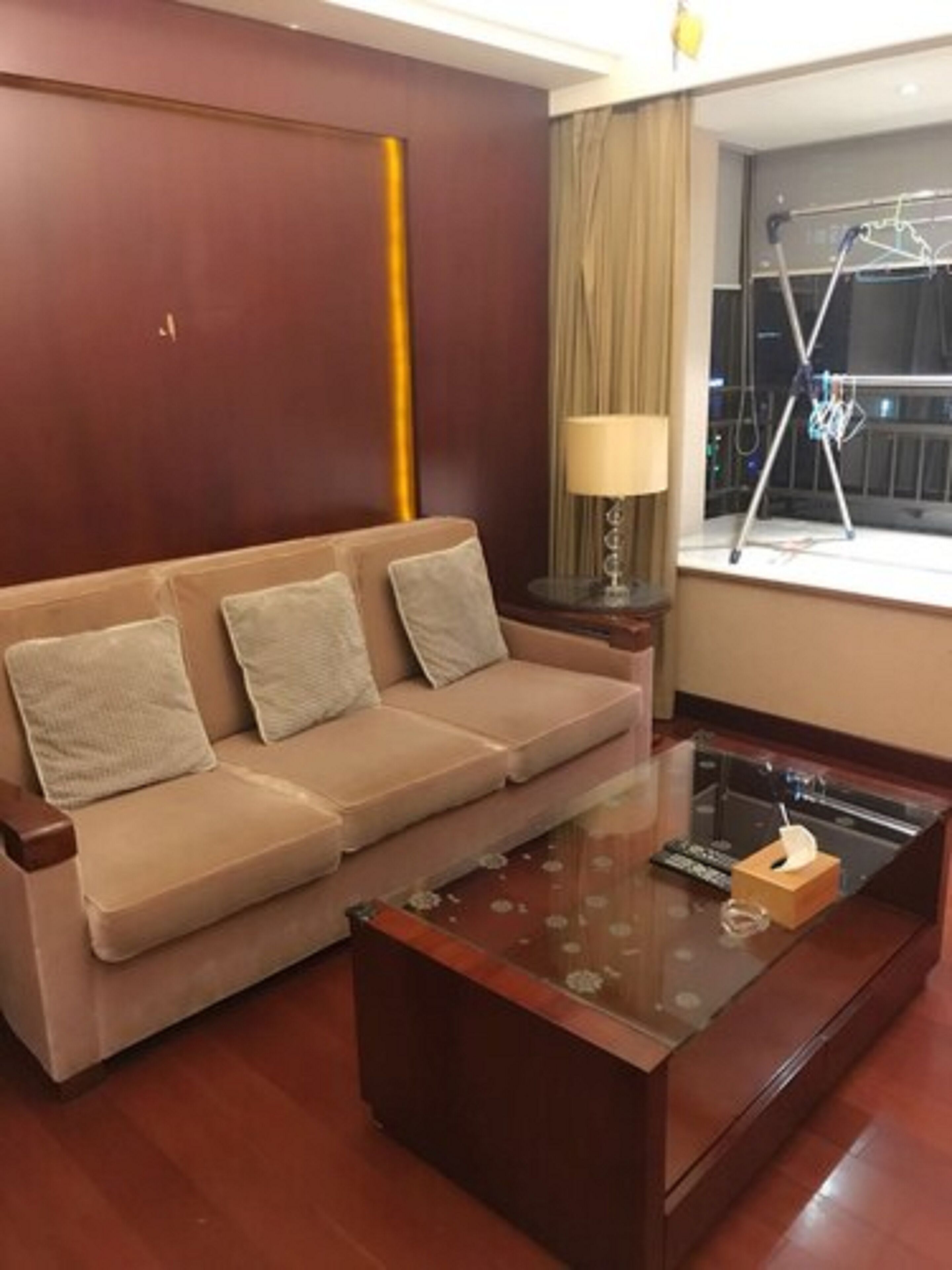 A living room with a beige sofa, a glass coffee table, a lamp, and a window with a balcony view.