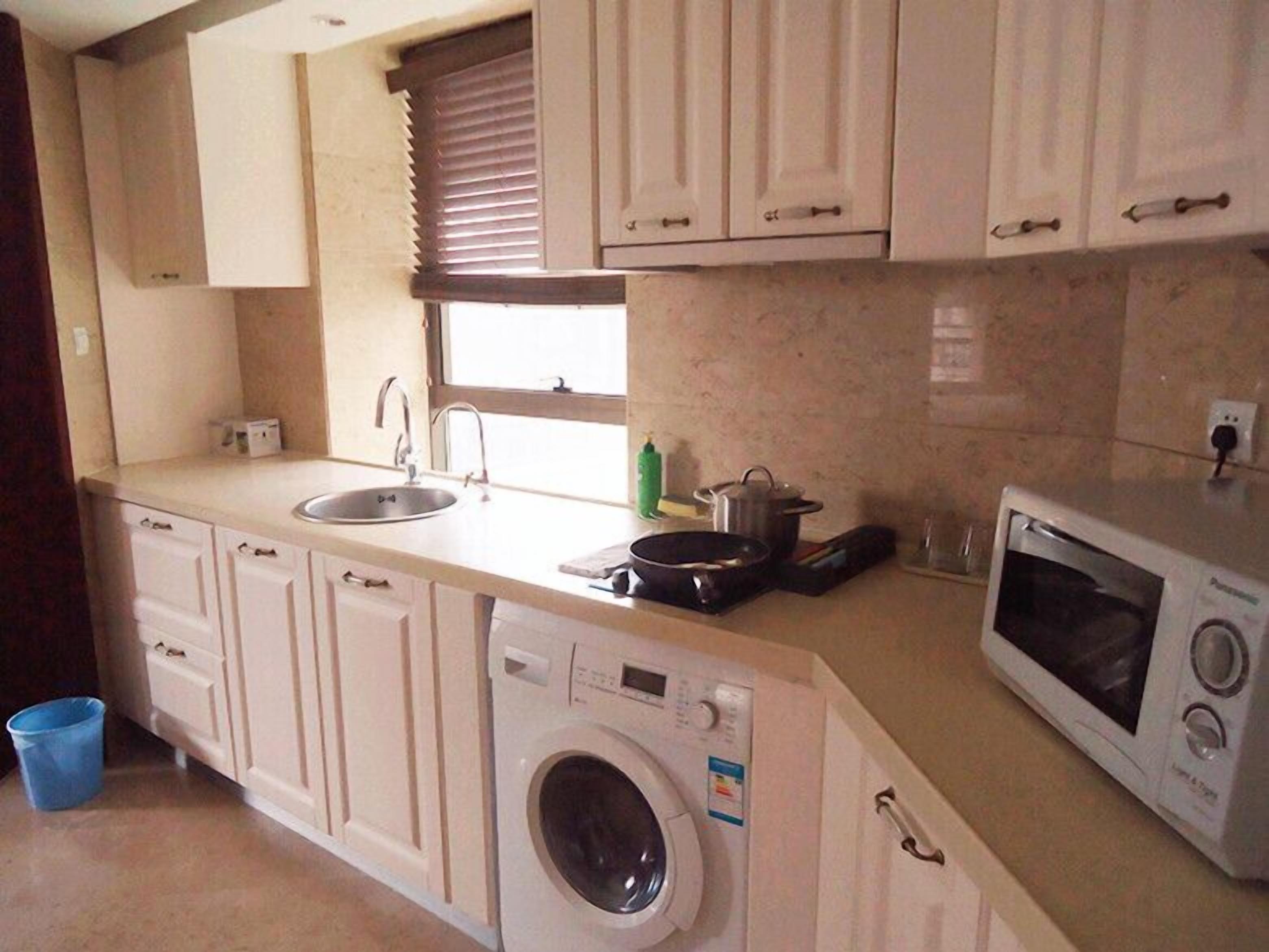 Cocina compacta con lavadora, microondas, fregadero y una ventana con persianas.