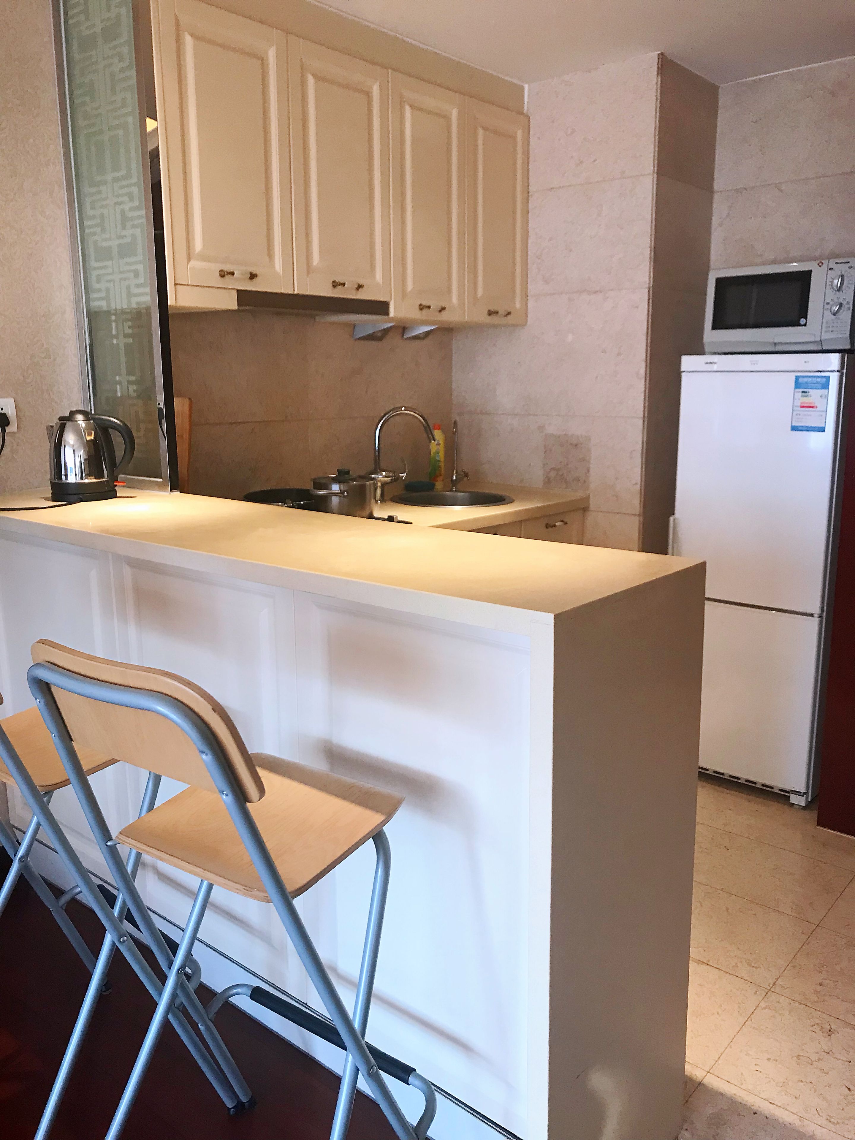 Uma cozinha compacta com armários brancos, micro-ondas embutido e geladeira.