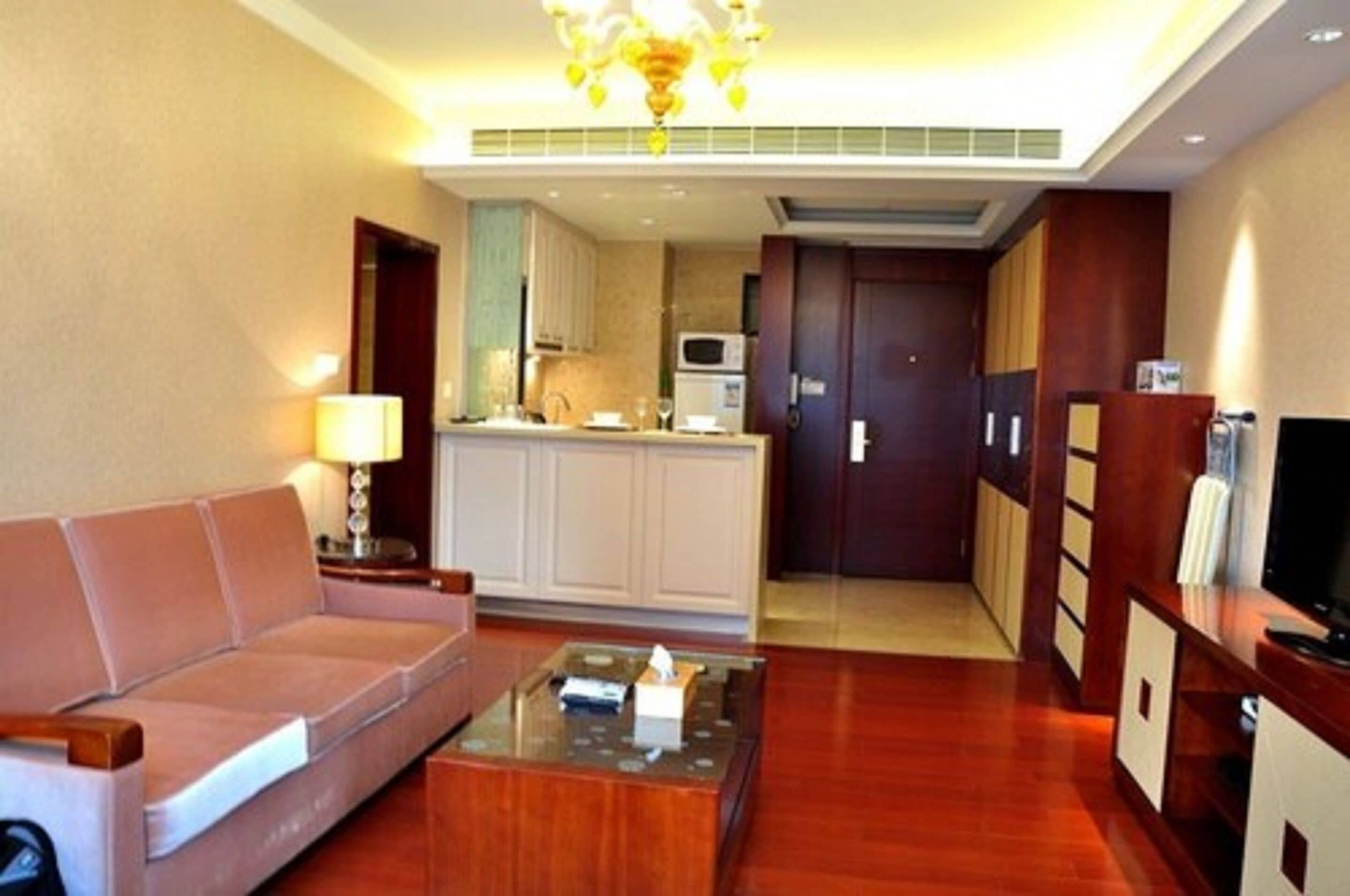 A hotel room with a sofa, a coffee table, a TV, a kitchenette, and a wooden cabinet.