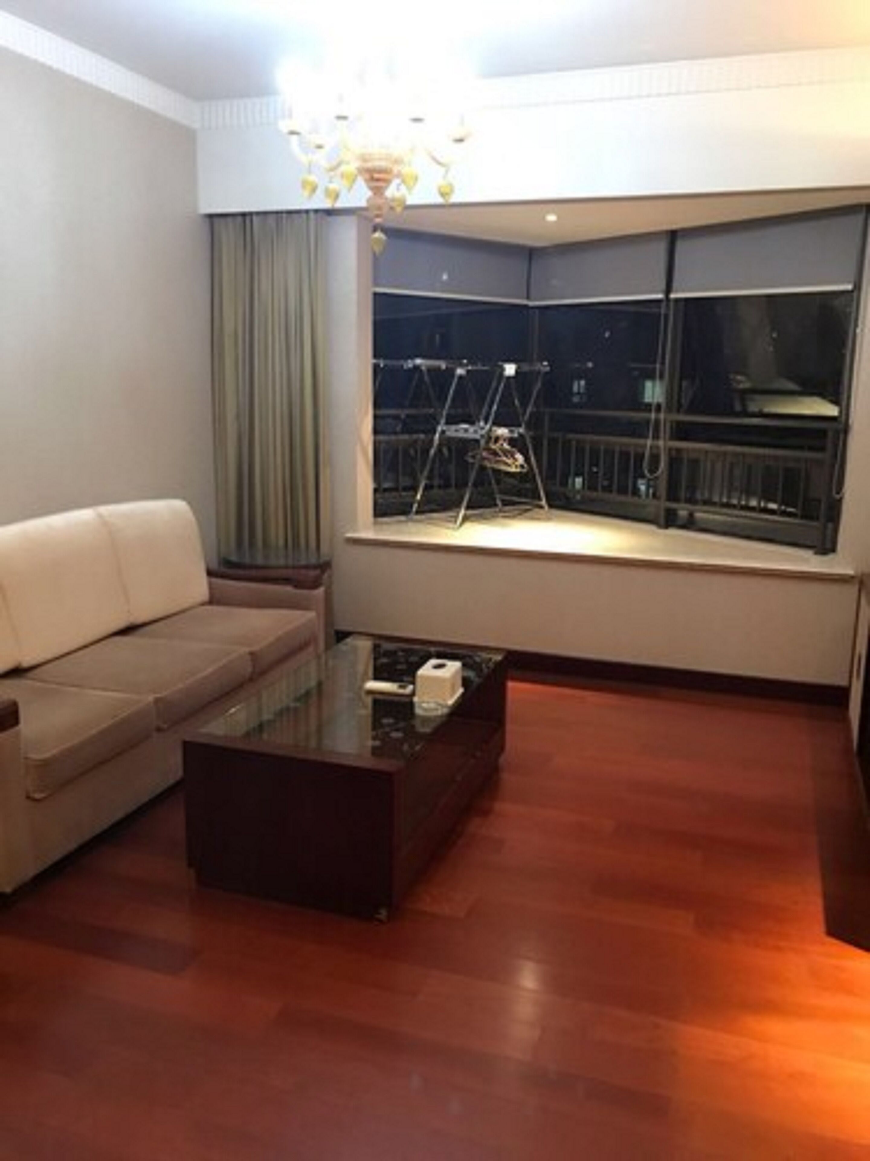 A living room with a sofa, a glass coffee table, and a large window with a view of the outside.