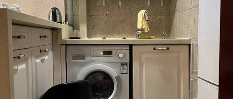 A compact kitchen with a washing machine, a sink, and a small stool.