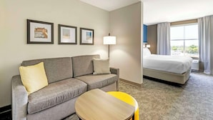Habitación de hotel con sofá gris, una pequeña mesa redonda, una cama y tres cuadros en la pared.
