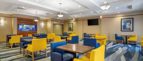 A hotel lobby with multiple seating areas, including booths and tables, and a bar area with a television.