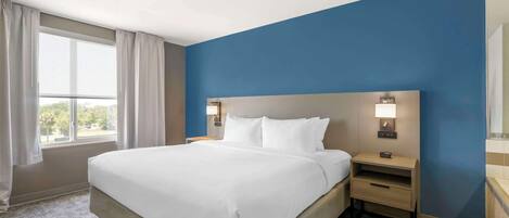 Habitación de hotel con una cama grande, dos mesitas de noche con lámparas, una ventana con cortinas y una pared azul decorativa.