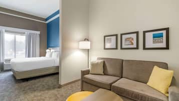 A hotel room with a bed, a sofa, a small table, and a lamp. There are three framed pictures on the wall.