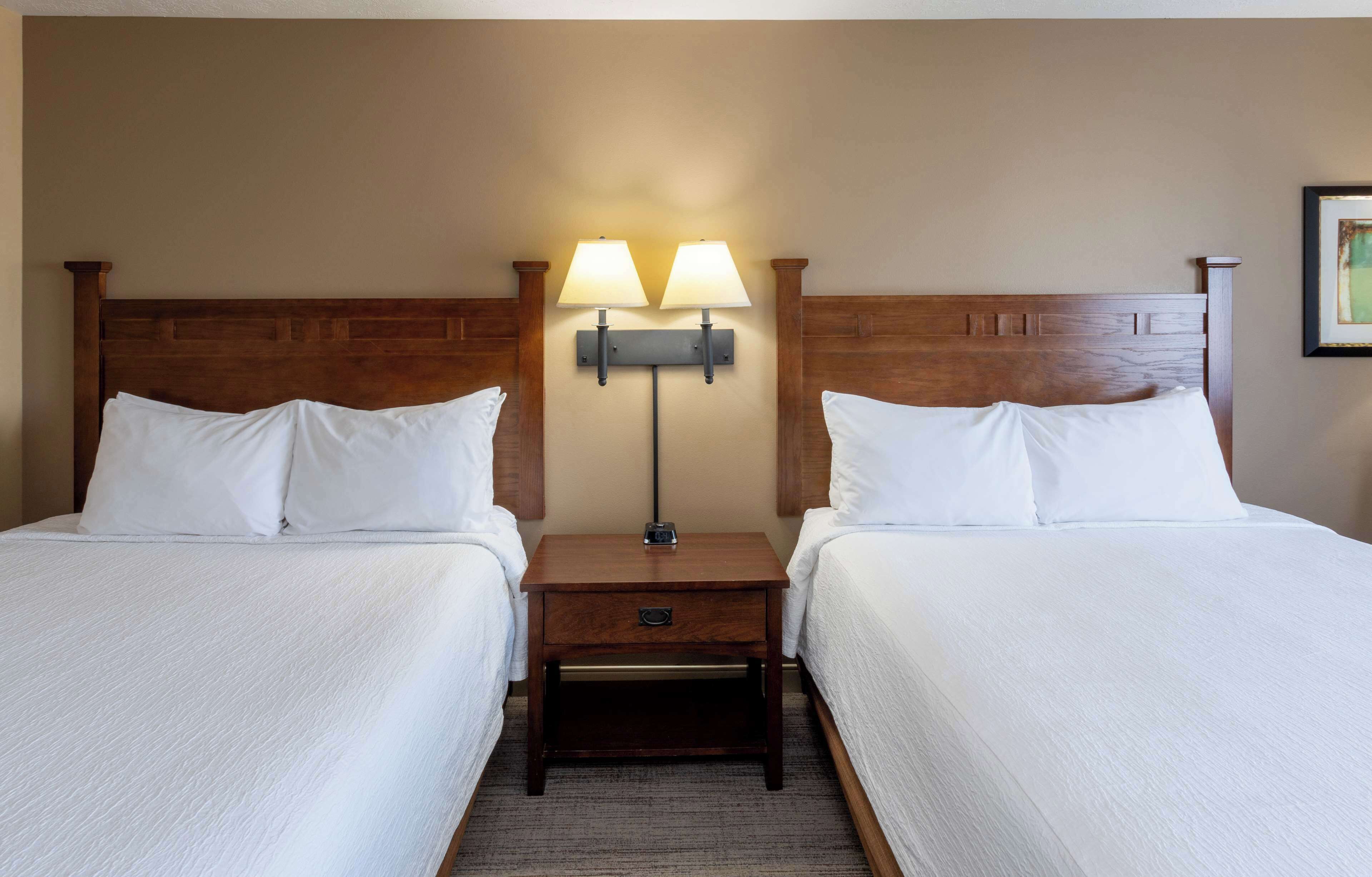 A hotel room with two beds, a nightstand with lamps, and a framed picture on the wall.