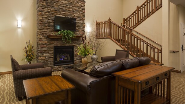 A living room with a stone fireplace, a wooden staircase, and a flat-screen TV mounted above it.