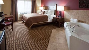 A hotel room with a bed, a desk, a chair, a desk lamp, a nightstand, a lamp, a bathroom with a bathtub, and a window with curtains.