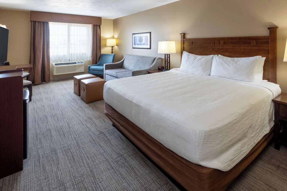 Une chambre d’hôtel avec un grand lit, un bureau, une chaise, une télévision et une fenêtre avec des rideaux.