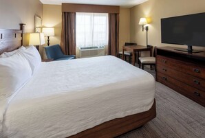 A hotel room with a large bed, a desk with a chair, a television, and a dresser.