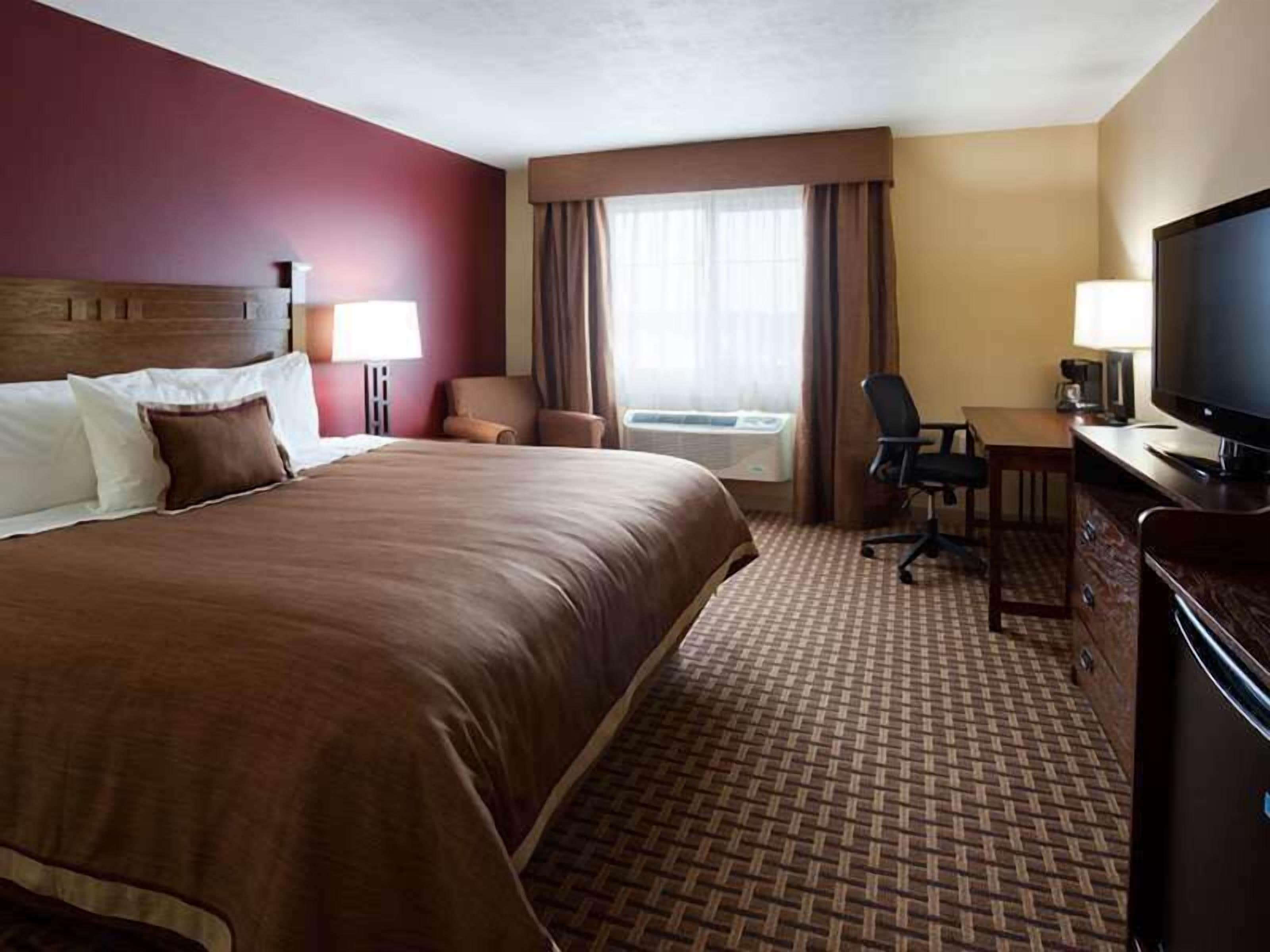 Une chambre d’hôtel avec un grand lit, un bureau avec une chaise, une télévision et une fenêtre avec des rideaux.
