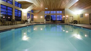 An indoor swimming pool with clear water, surrounded by windows and chairs.