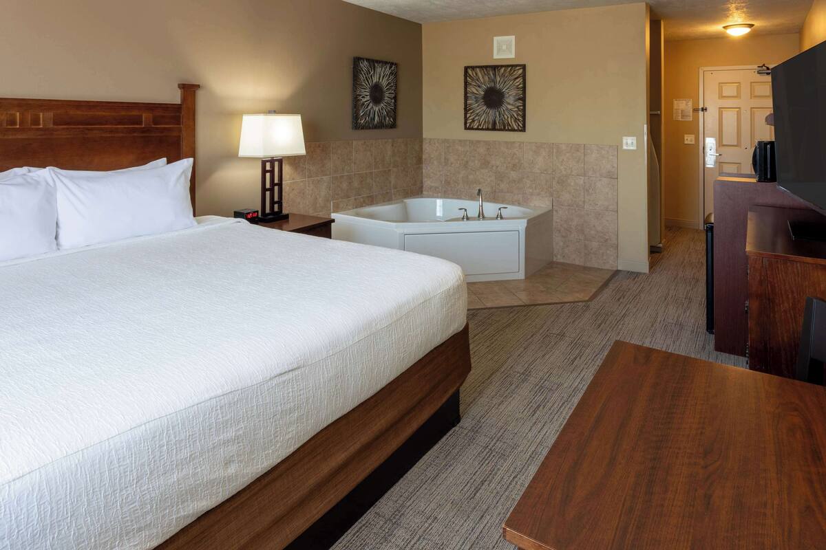 Une chambre d’hôtel avec un grand lit, une salle de bain séparée avec une baignoire, un bureau et une télévision.