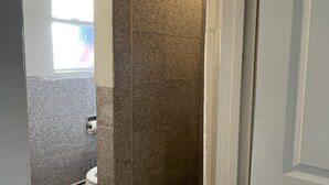 A bathroom with a shower, a toilet, and a window.
