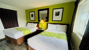 A hotel room with two beds, a nightstand with a lamp, a mirror, and framed pictures on the wall.