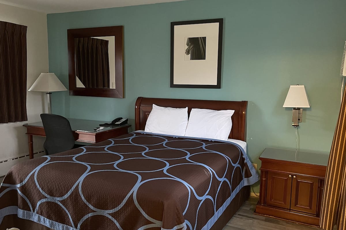 A hotel room with a large bed, a desk with a telephone, a chair, and a nightstand with a lamp.