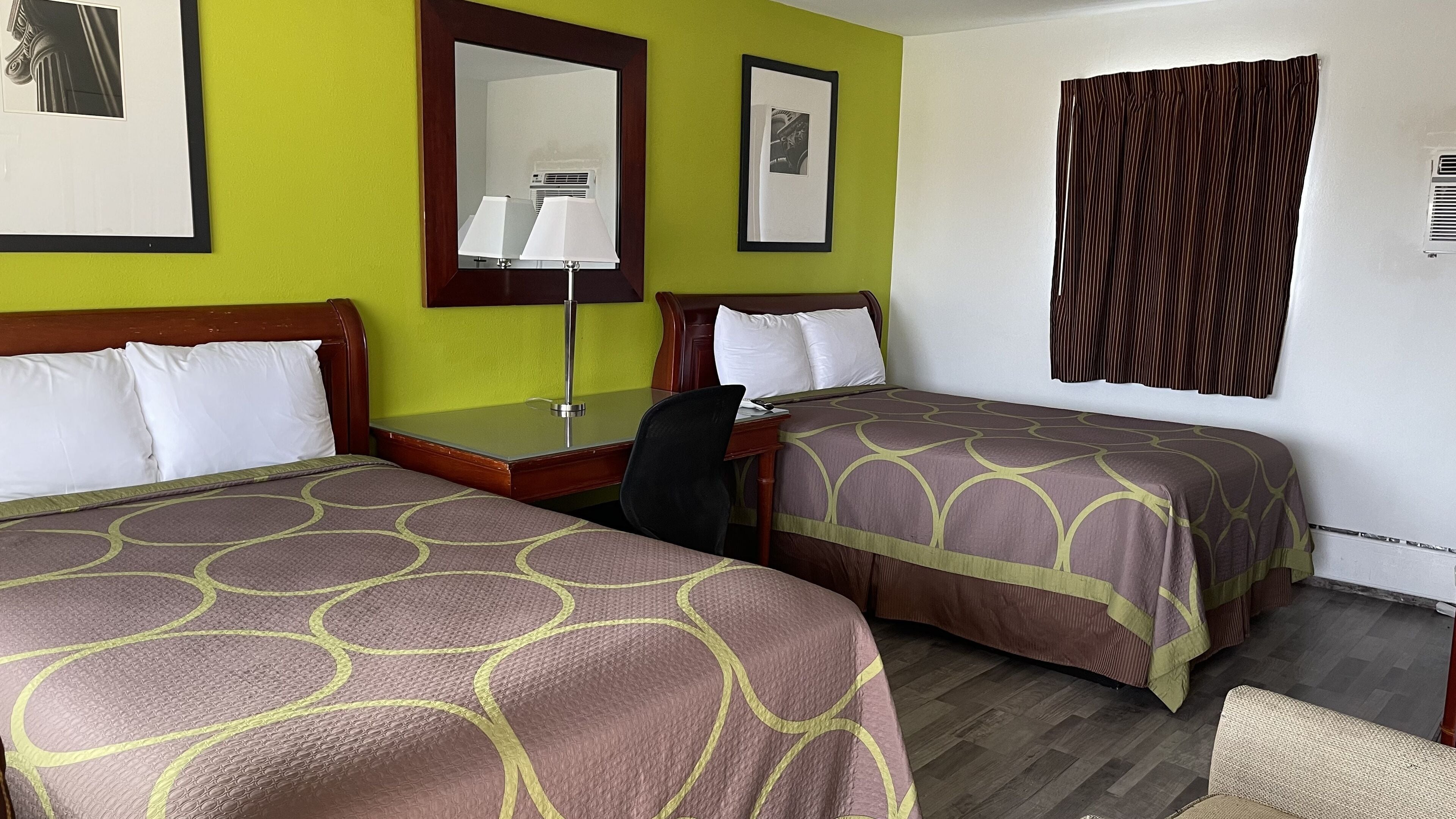 Habitación de hotel con dos camas, un escritorio, una silla, un espejo y una ventana con cortinas.