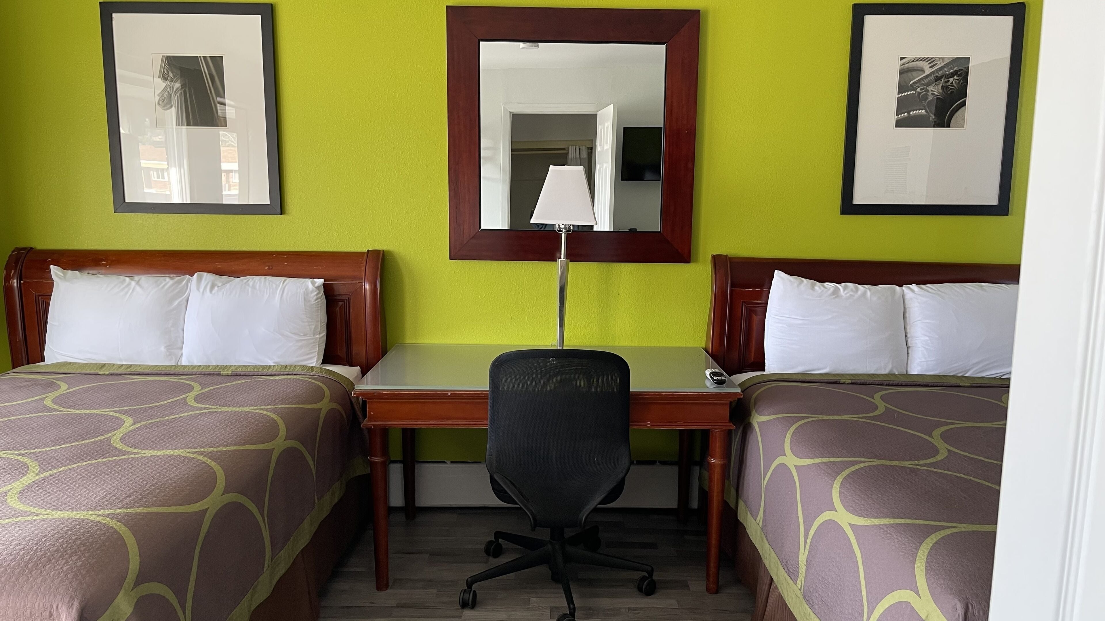 Habitación de hotel con dos camas individuales, un escritorio, una silla y un espejo.