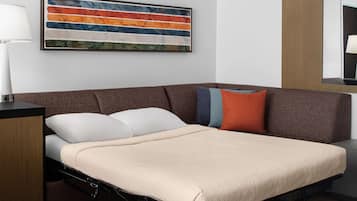 A modern room with a sofa bed, a side table, a lamp, and a colorful abstract painting.