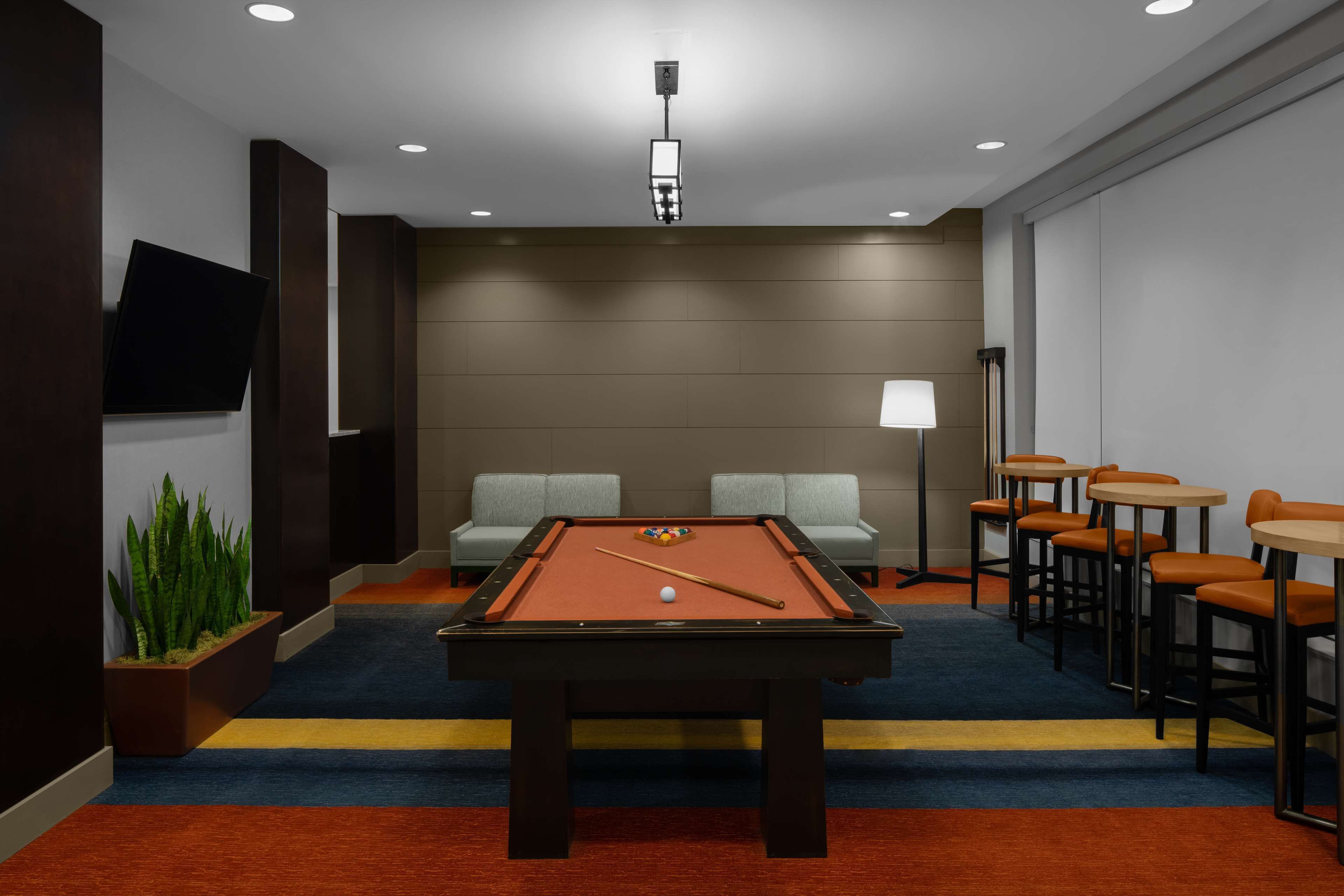 A pool table with a cue stick and balls, a sofa, and a bar area with stools.