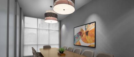 A conference room with a long wooden table, beige chairs, a potted plant, and a large abstract painting on the wall.