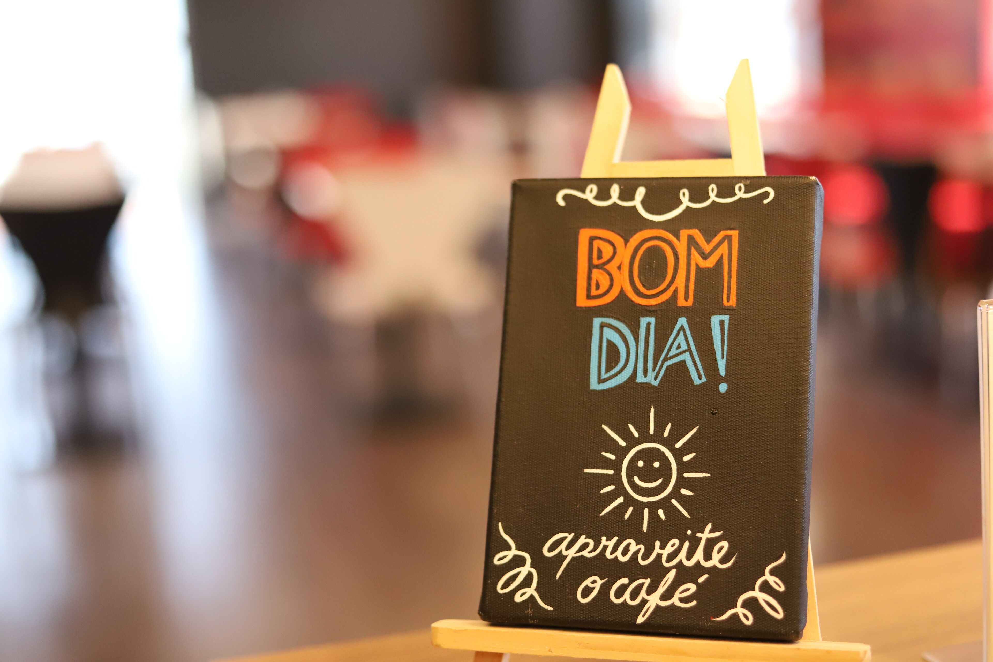A chalkboard sign with "BOM DIA!" and "aproveite o café" written on it.