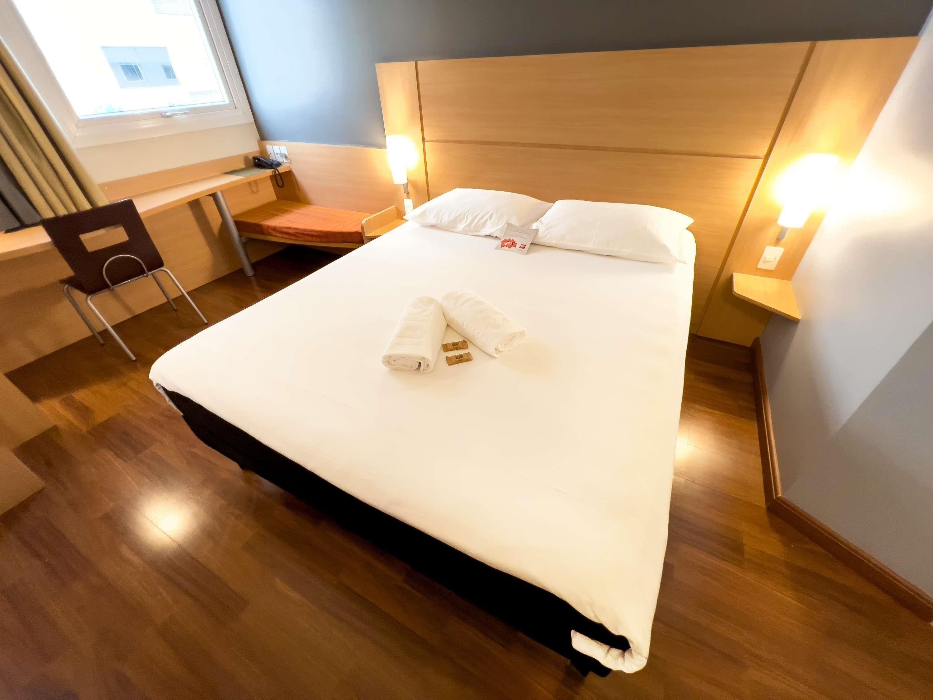 A hotel room with a bed, a desk, a chair, and a window.
