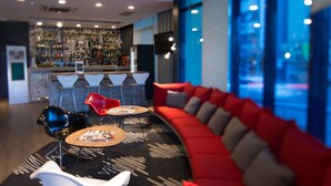 A modern lounge area with a curved red sofa, white and red chairs, and a bar area in the background. - ibis Passo Fundo Centro Hotel (Passo Fundo)