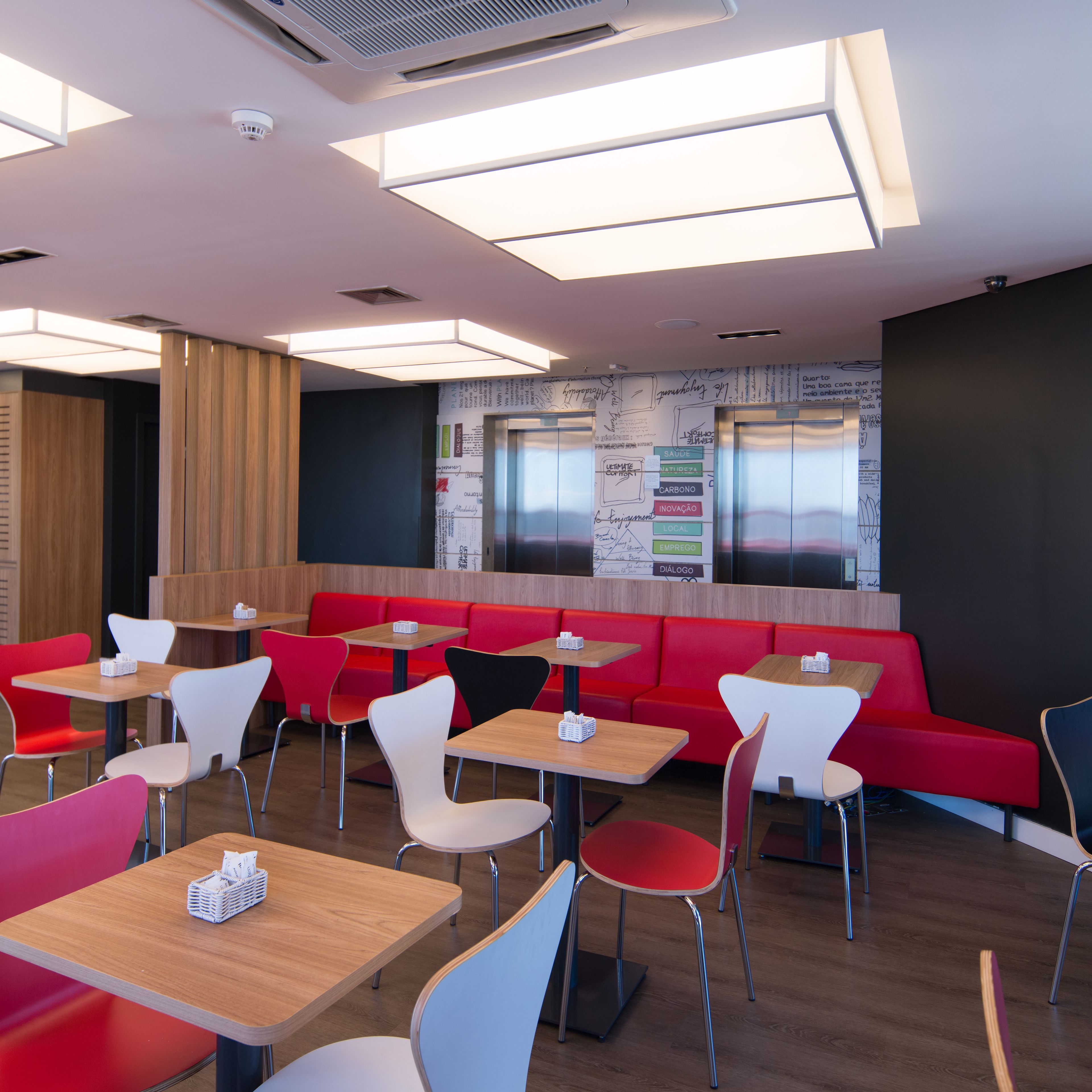 Un intérieur de restaurant moderne avec des sièges rouges et blancs, des tables en bois et un mur recouvert de notes manuscrites.