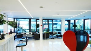 A modern lobby with a reception desk, seating area, and large windows. - AN HOTEL MILANO MELEGNANO (Carpiano)