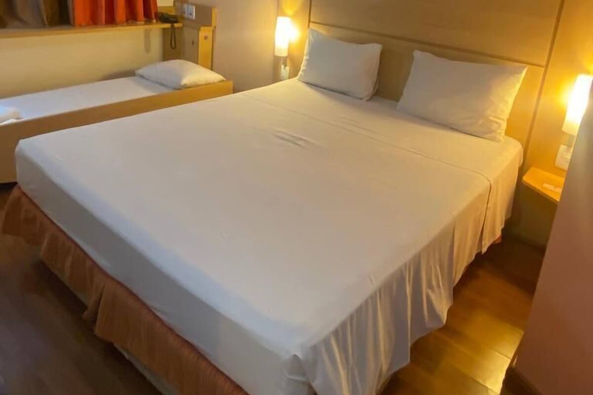 Ein Hotelzimmer mit einem großen Bett, zwei Nachttischen, einem Beistelltisch und einem Fenster mit Vorhängen.
