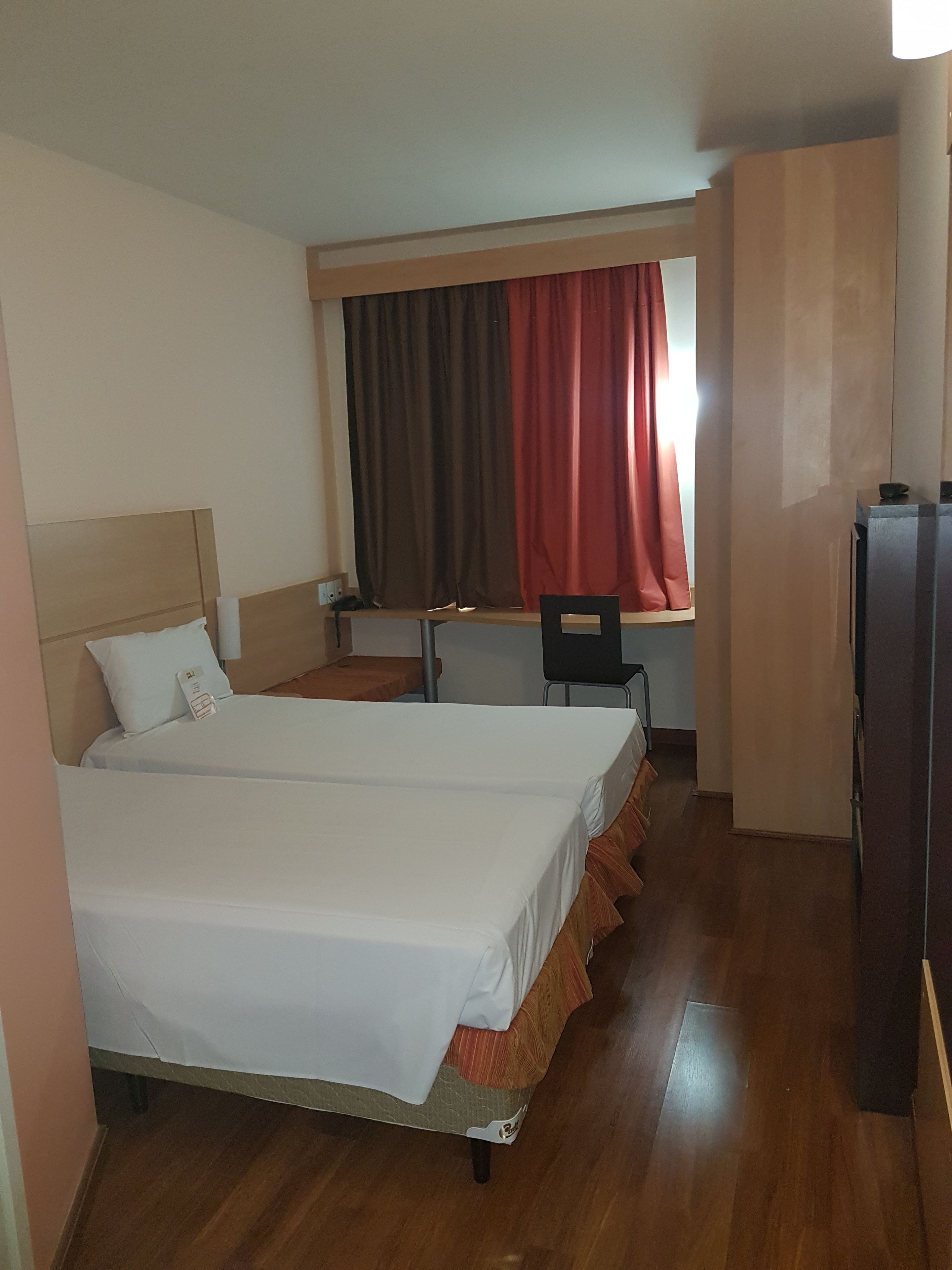 A hotel room with two beds, a desk, a chair, and a wardrobe.