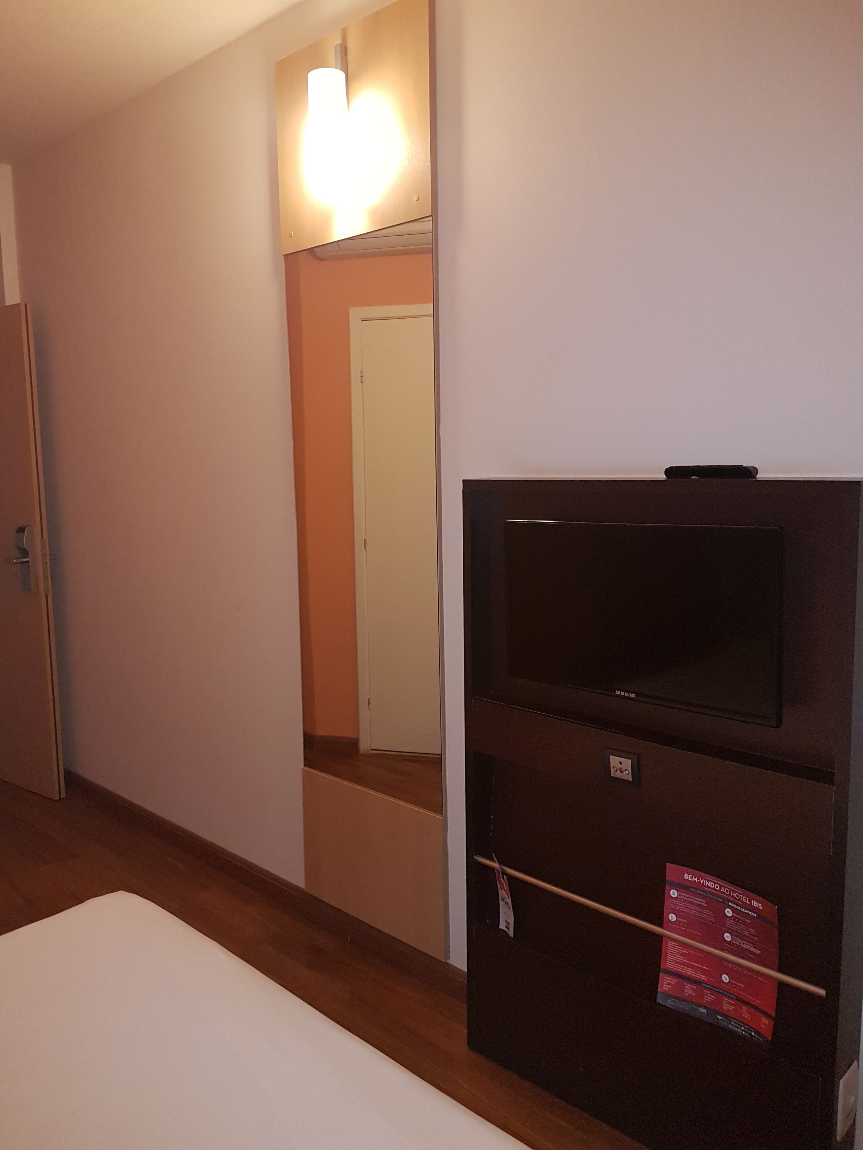 Een hotelkamer met een flatscreen televisie aan de muur, een houten vloer en een wit bed.