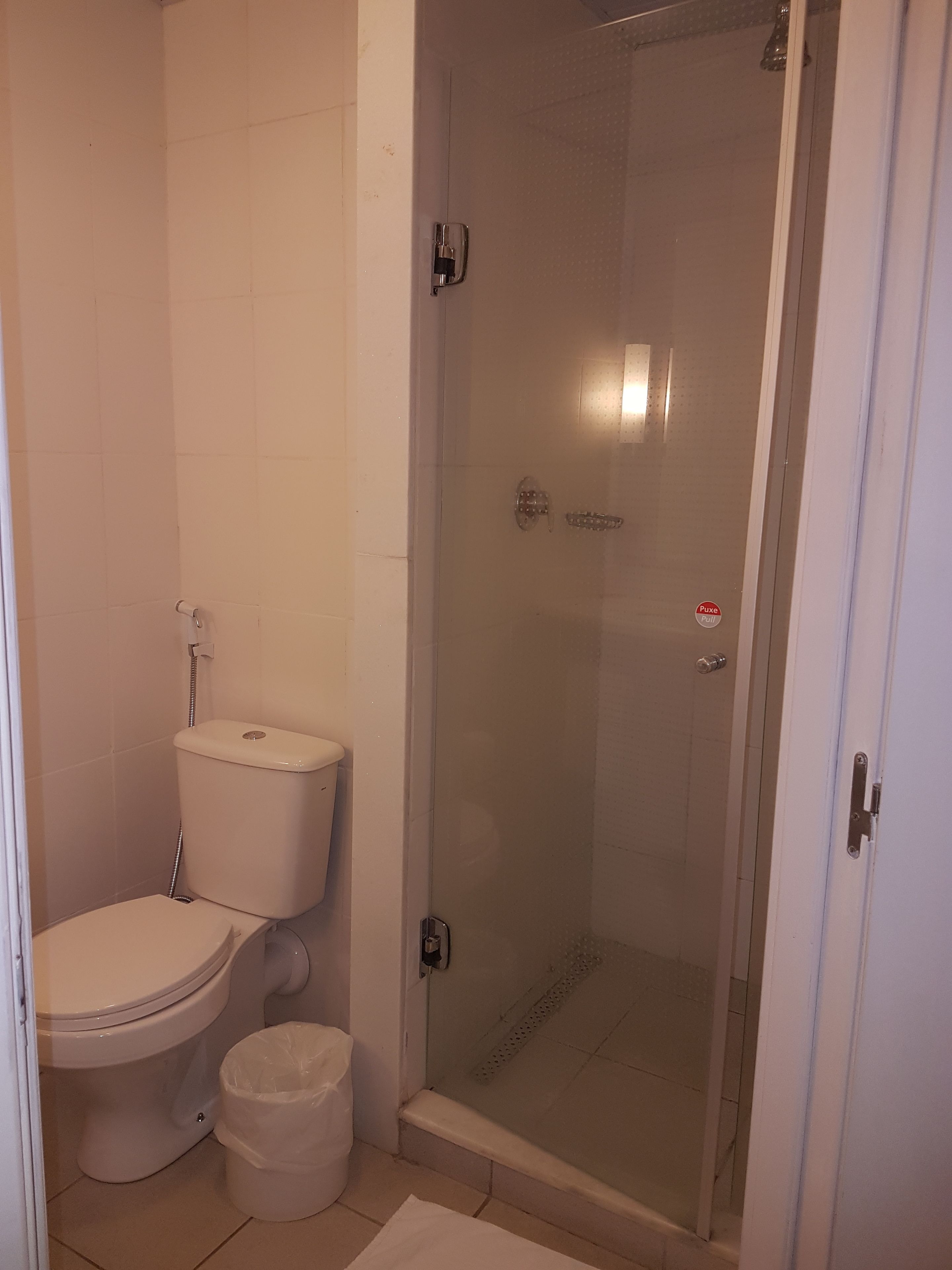 A bathroom with a toilet, a trash bin, and a glass-enclosed shower area.